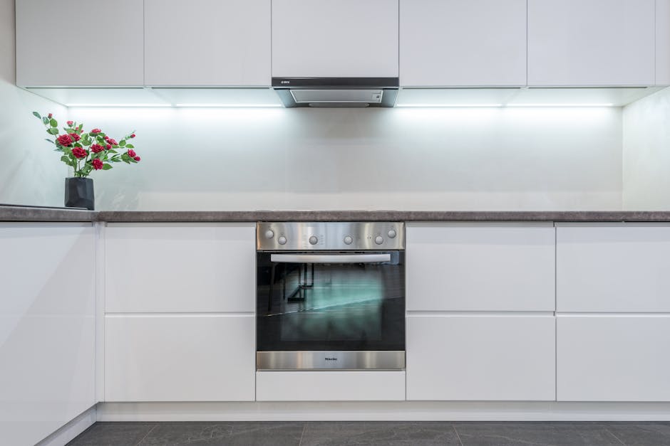 A close-up view of a stainless steel oven interior with a black surface, showing the process of surface cleaning. A worker's hand wearing a blue cleaning glove is wiping the oven's interior with a pur